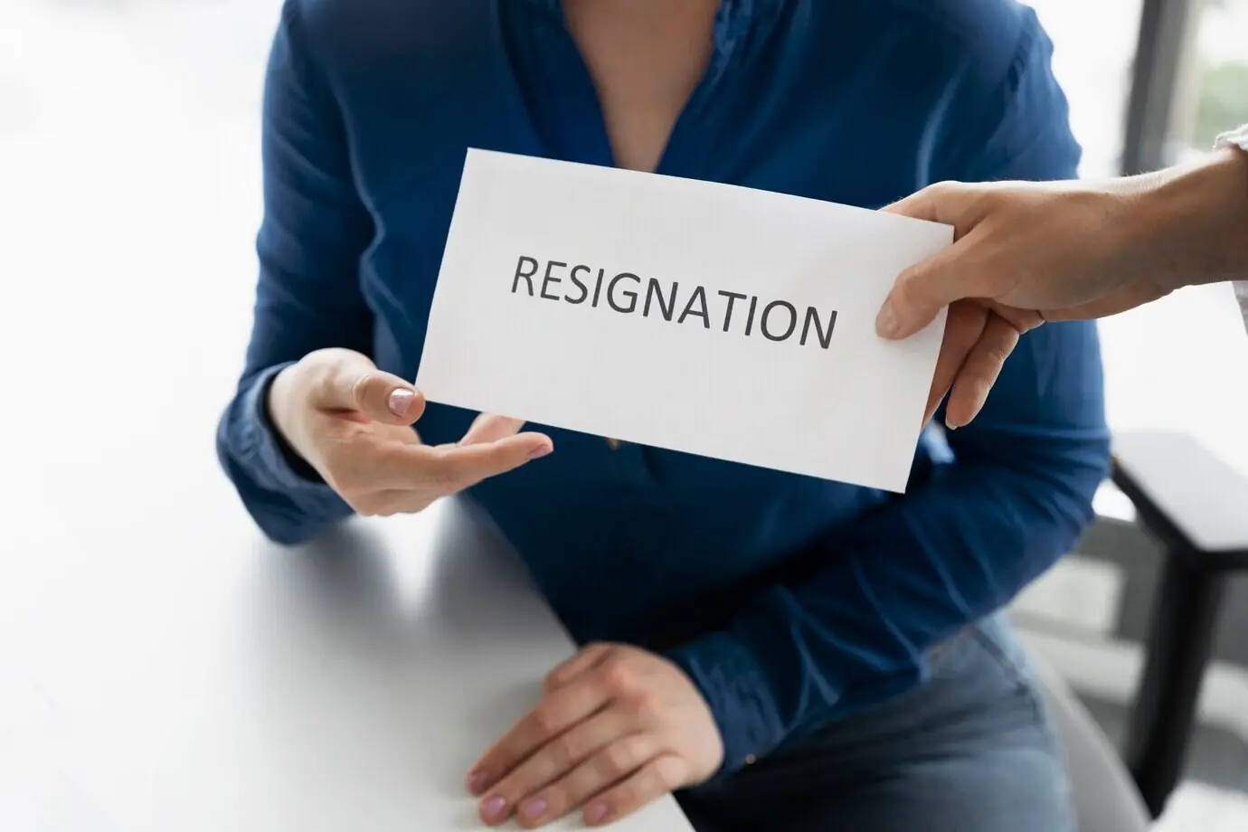 Вид сверху на руки, держащие записку об увольнении.